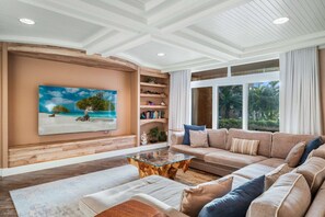 A living room with a large window, a sofa, a coffee table, and a bookshelf.