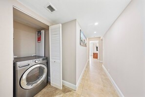 A laundry area with a washing machine and a dryer, a hallway with a door leading to another room, and a tiled floor.