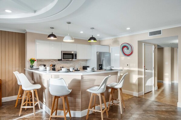 A modern kitchen with white cabinetry, a central island with bar stools, and pendant lighting.