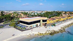 A coastal hotel with a beachside location, featuring a large building with a red roof, a pool area, and a sandy beach.