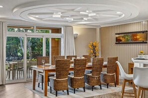 A dining area with wicker chairs, a wooden table, and a view through glass doors to an outdoor setting.