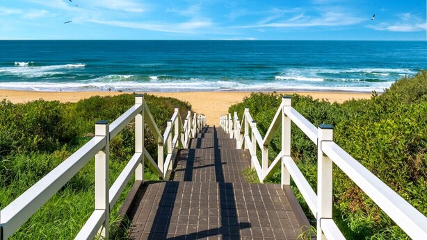 Un sendero que lleva a una playa con barandas blancas y vista al océano.