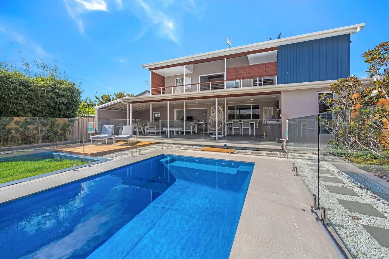 A modern two-story house with a swimming pool, outdoor seating, and a covered patio.