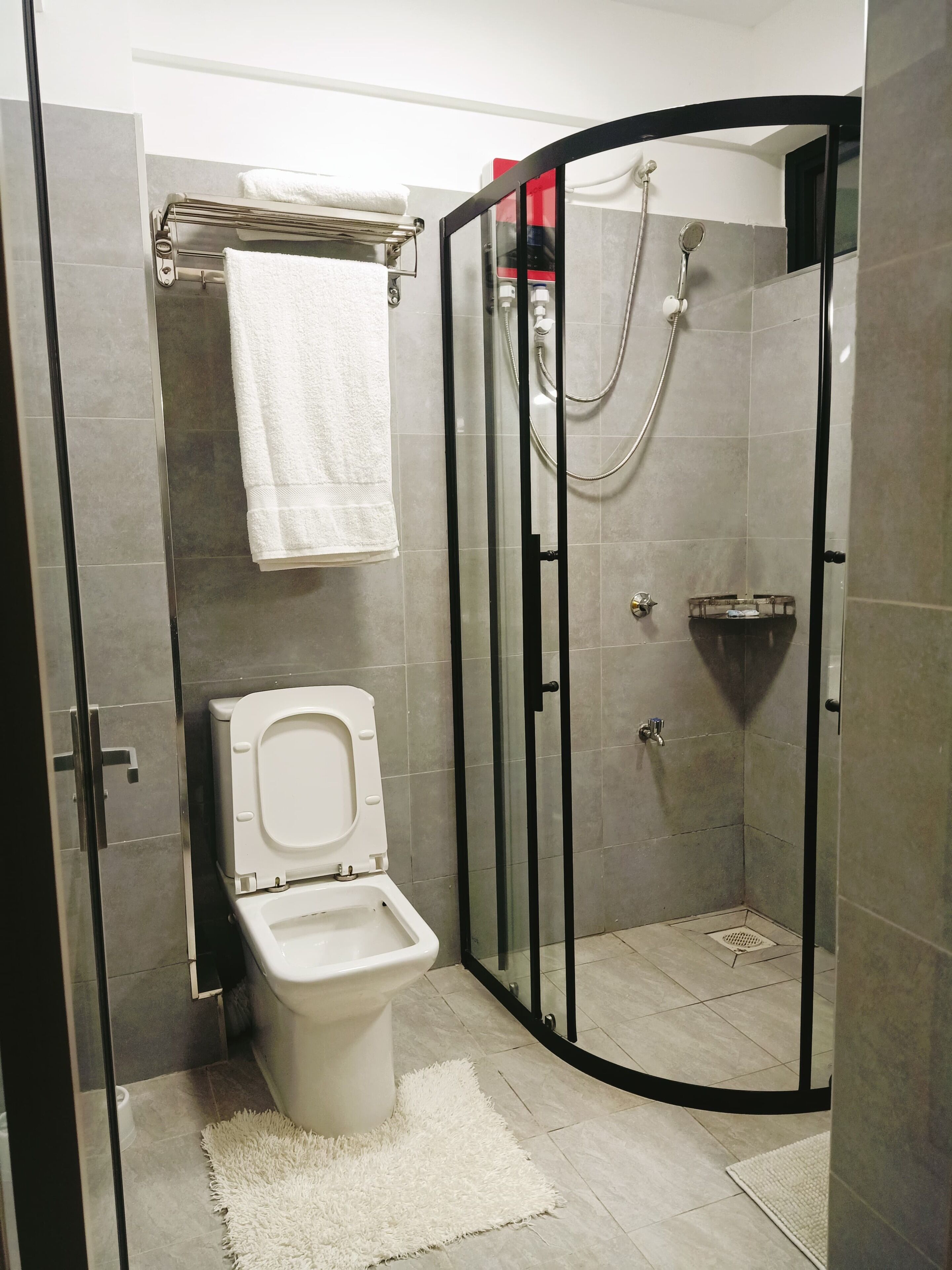 A modern bathroom with a toilet, a shower enclosure, and a towel rack.