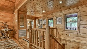 Interior de una cabaña de madera con escalera, paredes de madera y cuadros enmarcados.