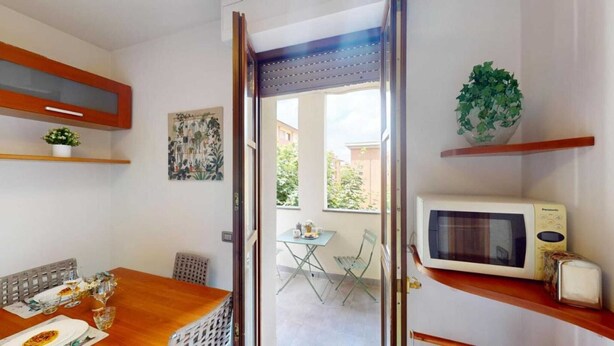 Un coin repas avec une table en bois, des chaises et un petit balcon offrant une vue sur les bâtiments.