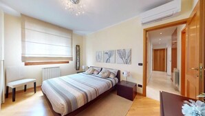 Une chambre à coucher avec un grand lit, des tables de chevet, un banc et des œuvres d’art accrochées au mur.