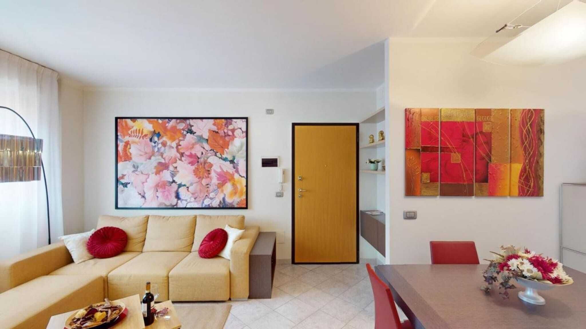 Una sala de estar moderna con un sofá color beige, una mesa de centro con una botella y un vaso, y un cuadro abstracto y llamativo sobre el sofá.