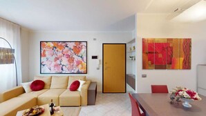 Un salon moderne avec un canapé beige, une table basse sur laquelle se trouvent une bouteille et un verre, et un tableau abstrait aux couleurs vives accroché au-dessus du canapé.