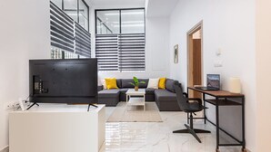 Una sala moderna con una televisión de pantalla plana, un sofá, una mesa de centro y un escritorio con una computadora.