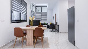 Un comedor moderno con una mesa de madera y sillas marrones, un sofá y un televisor al fondo.