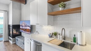 Une cuisine moderne avec des meubles blancs, un évier en acier inoxydable, des poutres en bois et une cheminée.