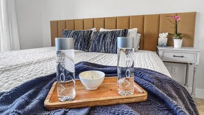 Un lit bien fait, sur lequel repose un plateau en bois contenant deux verres d’eau, un bol et une boîte de mouchoirs.