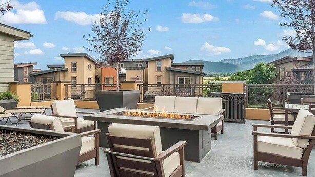 Une terrasse extérieure dotée d’un foyer, de sièges et offrant une vue sur les bâtiments voisins.