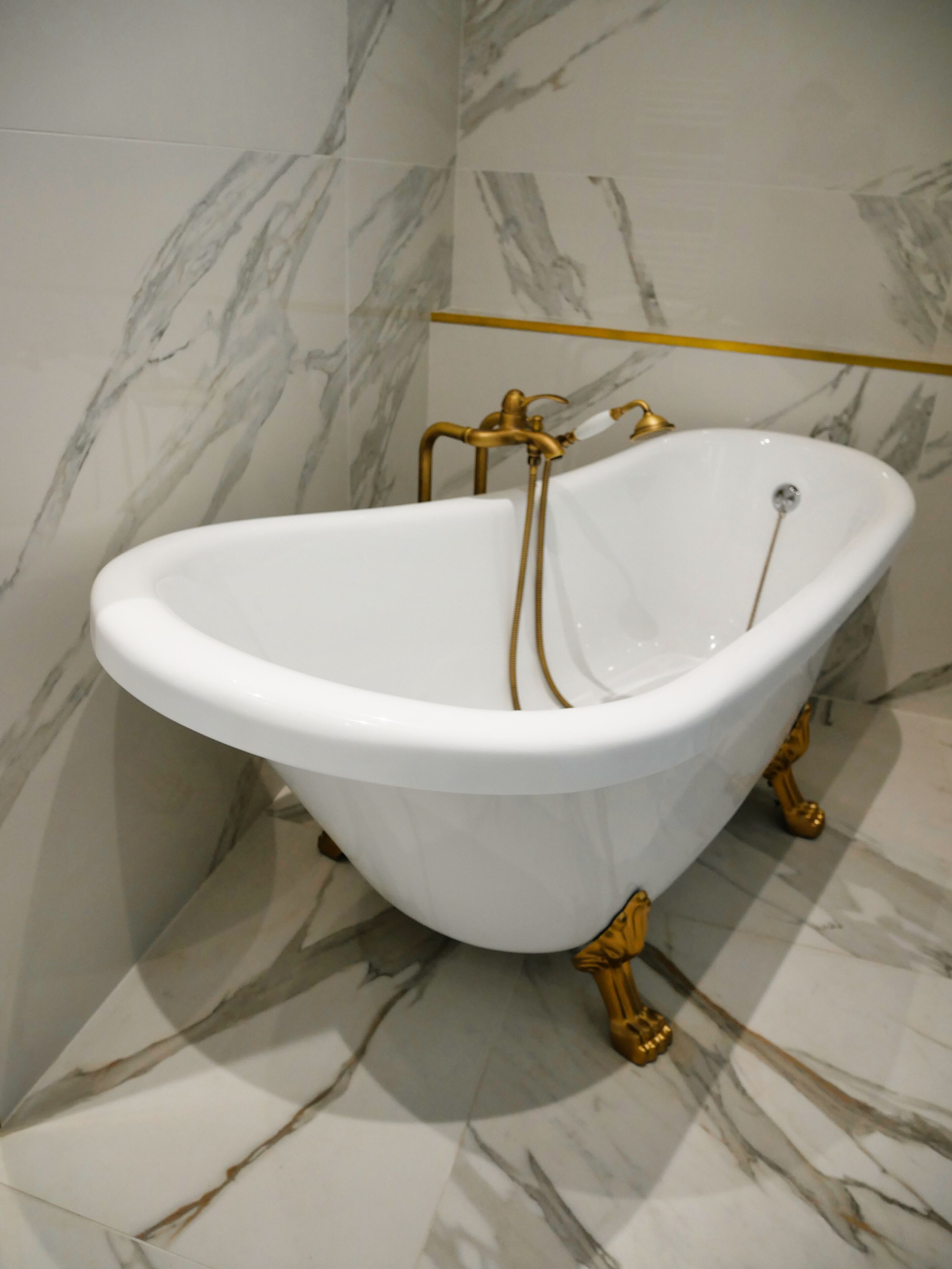 Una vasca da bagno indipendente con dettagli dorati in un bagno con pavimento e pareti in marmo.