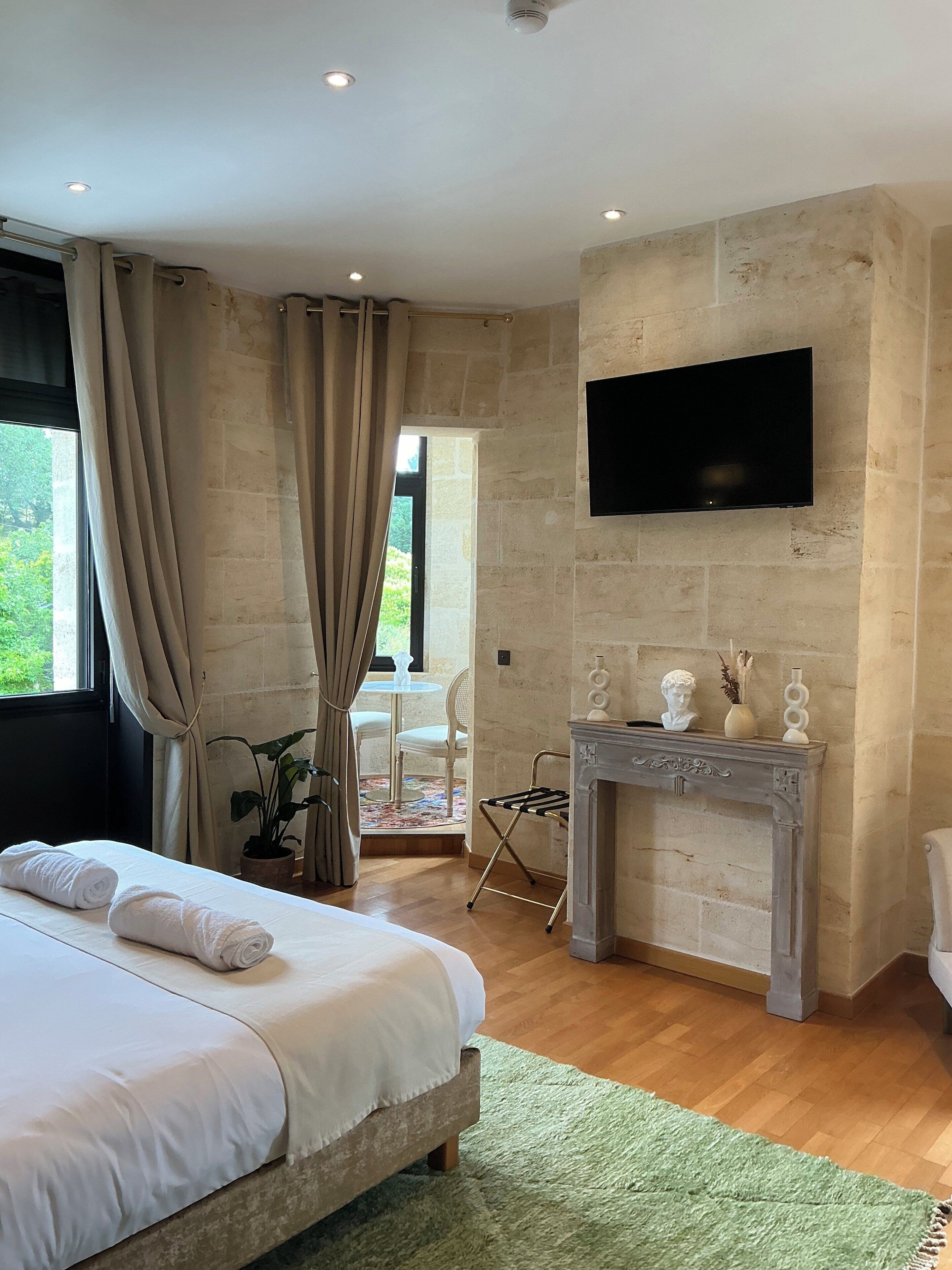 Un dormitorio con cama, chimenea, televisor y vistas al exterior.