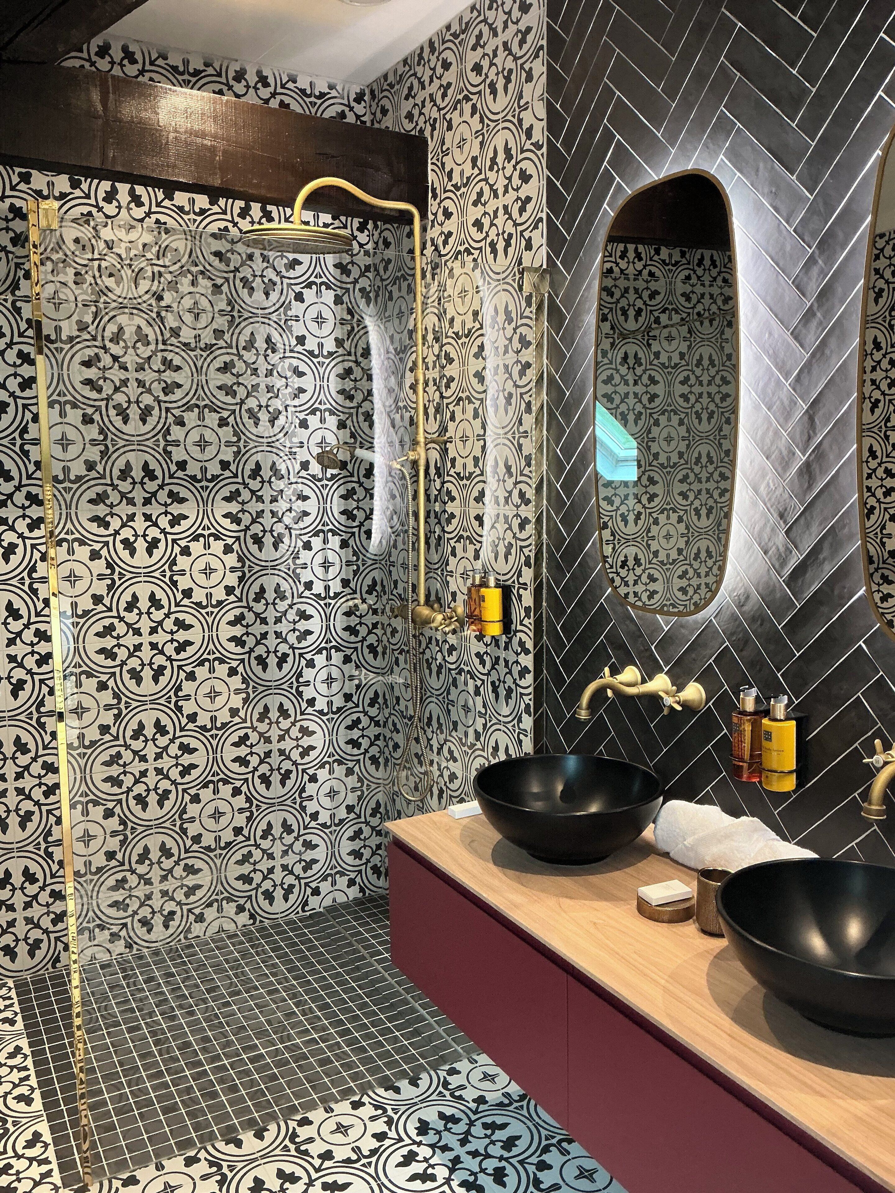 A bathroom with patterned tiles, a black sink, and a mirror with a unique arch design.
