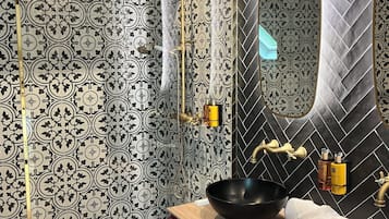 A bathroom with patterned tiles, a black sink, and a mirror with a unique arch design.