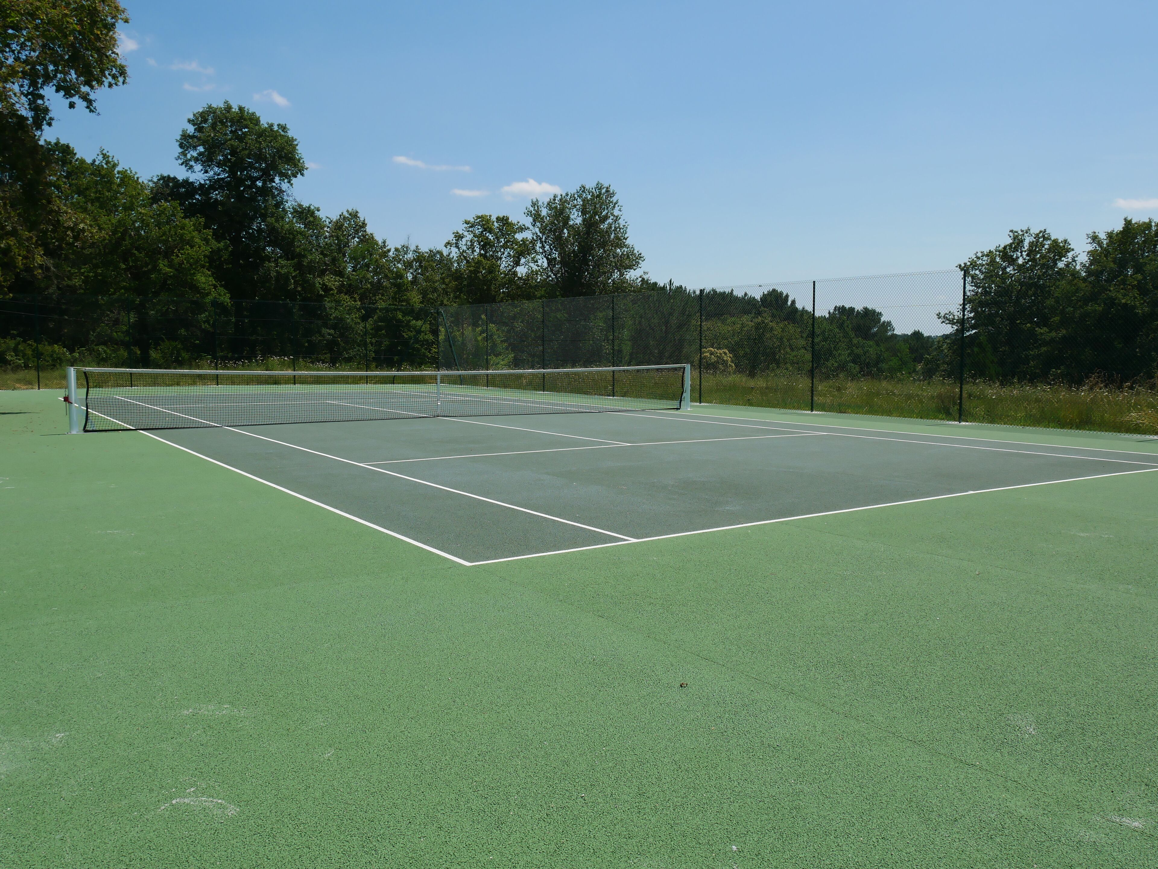 A tennis court with a net, surrounded by trees and a fence.