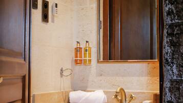 A bathroom with a wooden vanity, a sink with a gold faucet, a towel, and two bottles of toiletries on the wall.