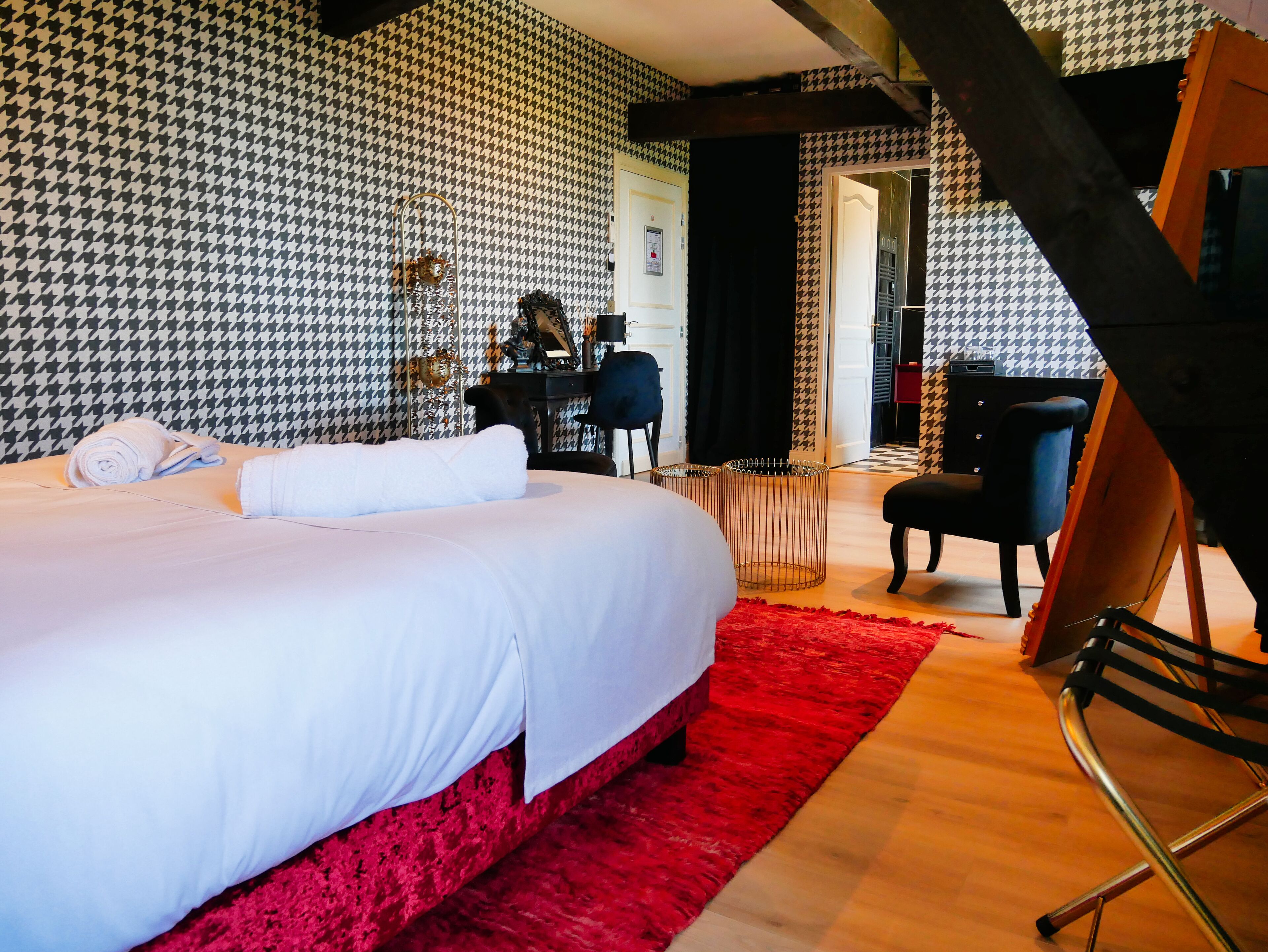 A hotel room with a large bed, a red rug, a desk with a chair, and a houndstooth patterned wall.