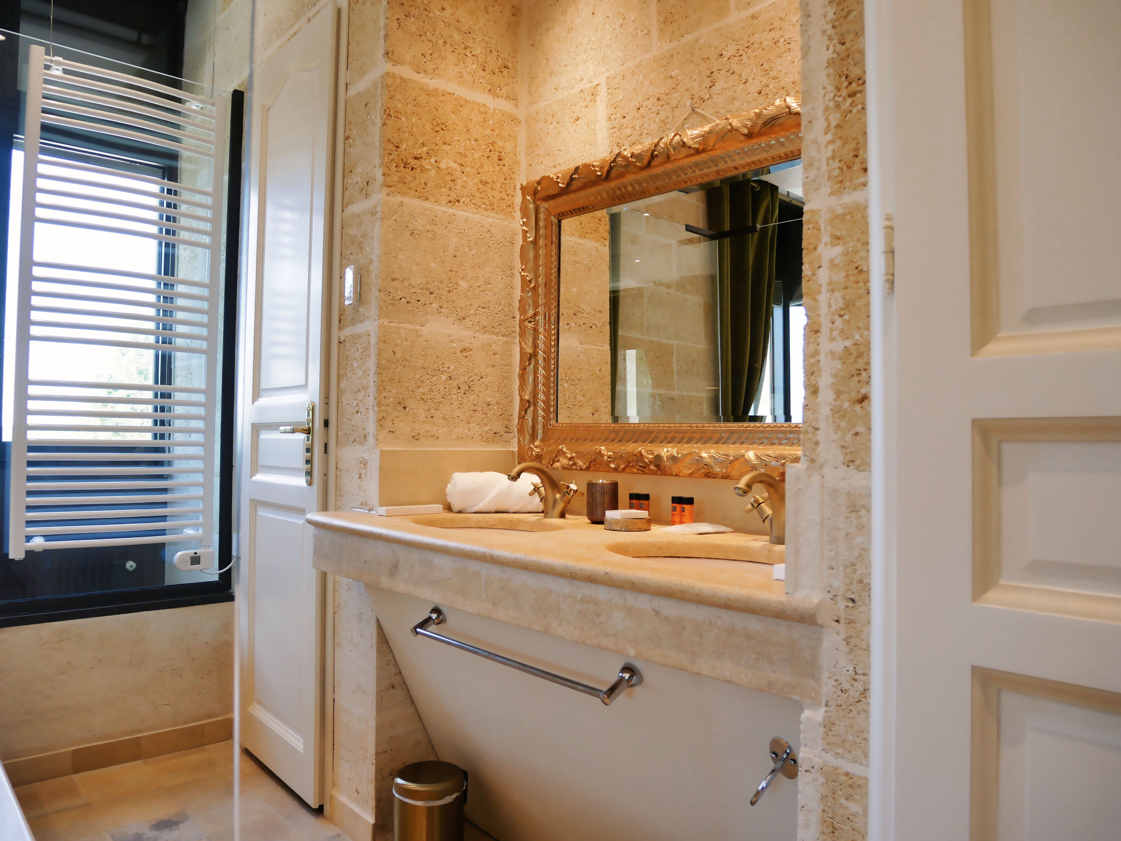 A bathroom with a beige tiled wall, a gold-framed mirror, a sink with a towel, and a handrail.