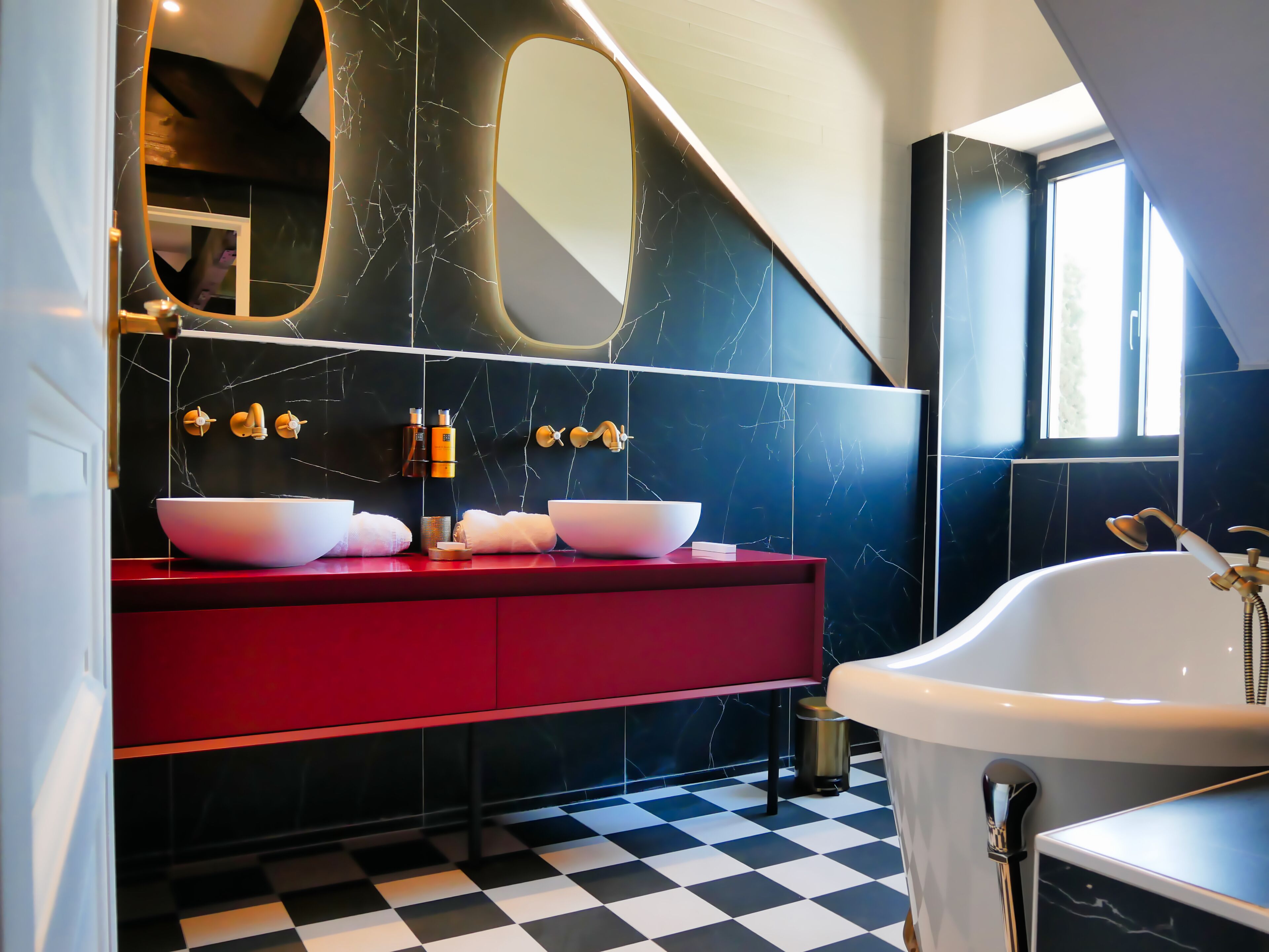A modern bathroom with a red vanity, two large white bowls, a white bathtub, and a large mirror.