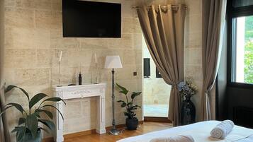 A bedroom with a large bed, a desk, a chair, a TV mounted on the wall, and a window with curtains.