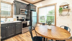 A modern kitchen with dark cabinets, stainless steel appliances, and a wooden dining table.