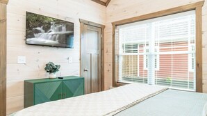 A bedroom with a bed, a TV mounted on the wall, a window with blinds, and a green cabinet.