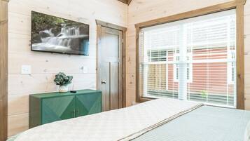A bedroom with a bed, a TV mounted on the wall, a window with blinds, and a green cabinet.