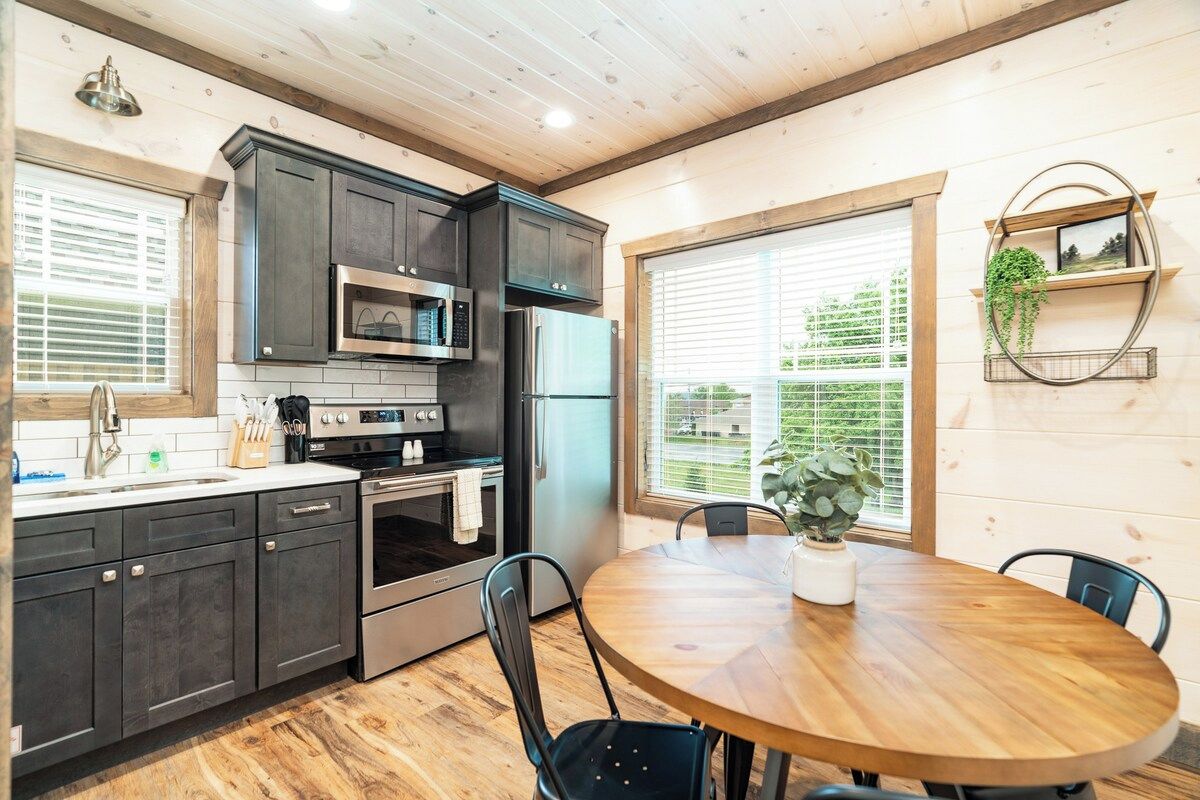 A modern kitchen with dark cabinetry, stainless steel appliances, and a round wooden dining table.