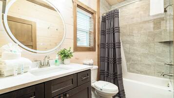 A bathroom with a wooden vanity, a large mirror, a toilet, and a bathtub.