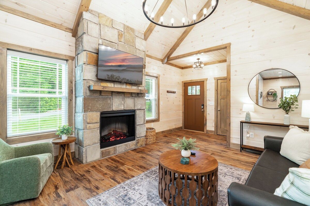 A cozy living room with a stone fireplace, a flat-screen TV mounted above it, and a comfortable seating area with a couch and a round coffee table.
