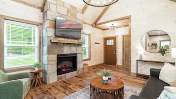A cozy living room with a stone fireplace, a flat-screen TV mounted above it, and a comfortable seating area with a couch and a round coffee table.