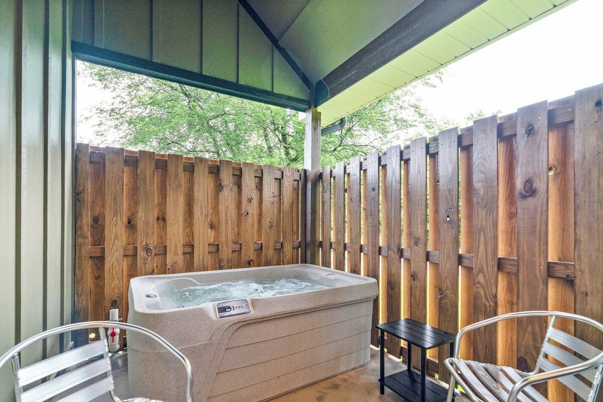 Een hottub onder een overdekte veranda met houten omheining, twee stoelen en een bijzettafeltje.