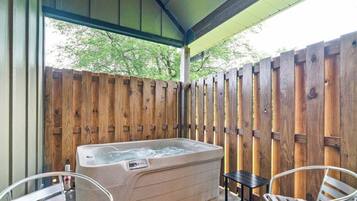 Een hottub onder een overdekte veranda met houten omheining, twee stoelen en een bijzettafeltje.