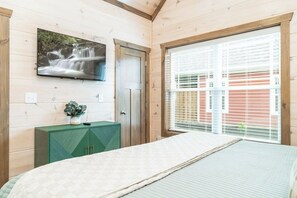 A bedroom with a bed, a television mounted on the wall, a window with blinds, and a green cabinet. - In Downtown Pigeon Forge/Hot Tub (Pigeon Forge)