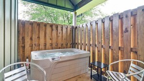 A hot tub under a covered patio with wooden fencing, two metal chairs, and a small table.