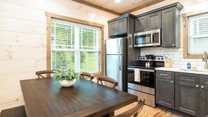 A kitchen with dark cabinets, stainless steel appliances, and a wooden dining table with chairs.