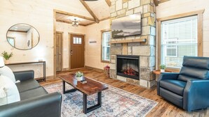 A cozy living room with a fireplace, wooden walls, a sofa, a coffee table, and a blue chair.