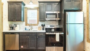 Une cuisine moderne avec des meubles de couleur sombre, des appareils électroménagers en acier inoxydable et un plancher en bois.