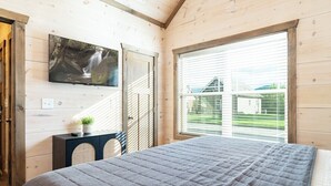 Une chambre à coucher avec un lit, un téléviseur fixé au mur, une fenêtre avec des stores et une petite table sur laquelle est posée une plante.