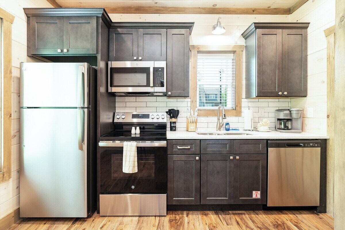 A modern kitchen with dark cabinets, stainless steel appliances, and a window with blinds.