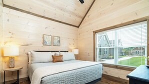 Ein Schlafzimmer mit einem großen Bett, Holzwänden, einem Fenster mit Jalousien und Blick auf ein Haus.