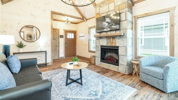 Ein geräumiges Wohnzimmer mit Kamin aus Stein, Holzbalken und einem großen Fenster.