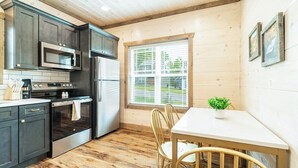 Una cocina con armarios oscuros, electrodomésticos de acero inoxidable, una ventana con persianas y una zona de comedor con mesa y sillas.