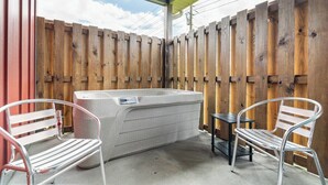 Un patio con un jacuzzi, dos sillas de metal y una mesita.