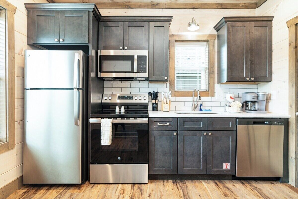 A modern kitchen with stainless steel appliances, dark cabinetry, and a wooden floor.