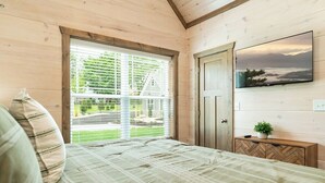 A bedroom with a bed, a window with blinds, a door, and a mounted TV.